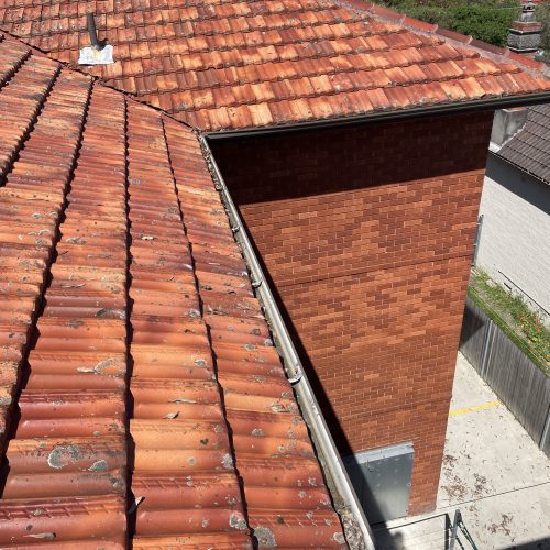 Terracotta tiled roof and gutter running beside a red-brick wall