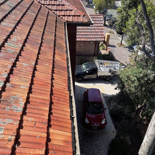 Terracotta tiled roof and gutter edge above a driveway with a ute and a red car